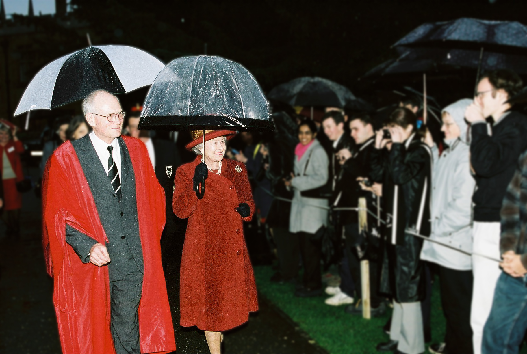 The queen with an umbrella at Trinity Hall in Cambridge. Smiling students line the path as she walks past.