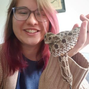 Woman is smiling and holding up a snake