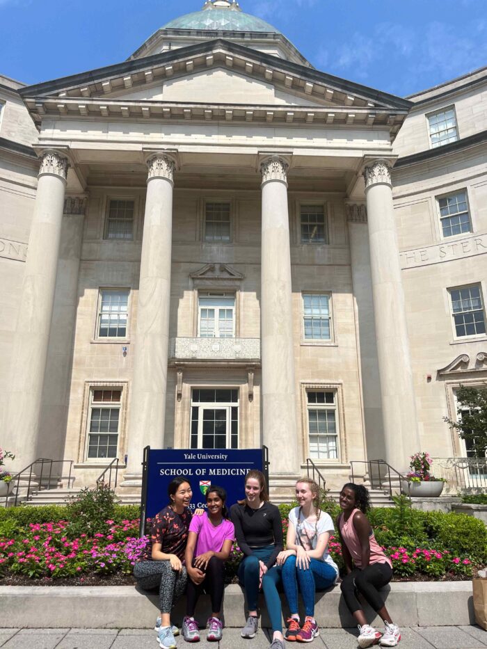 five students sit outside an old, classical building. It is the Yale University School of Medicine and they are Trinity Hall undergraduates.