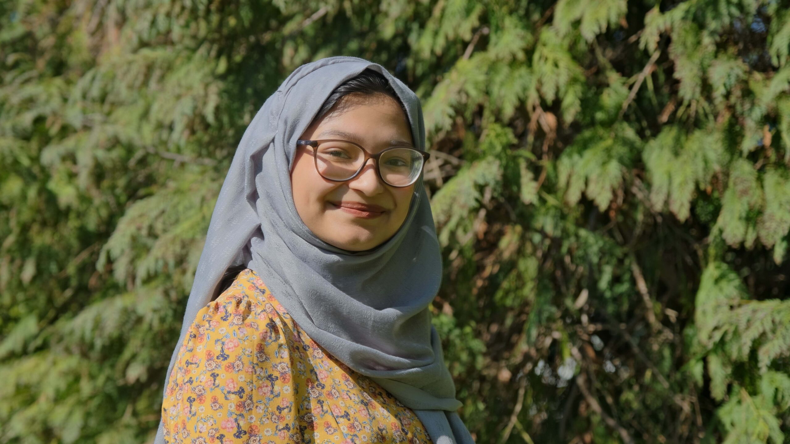 A woman smiling with trees behind her. She is undergraduate Trinity Hall student Umayyah Rahman
