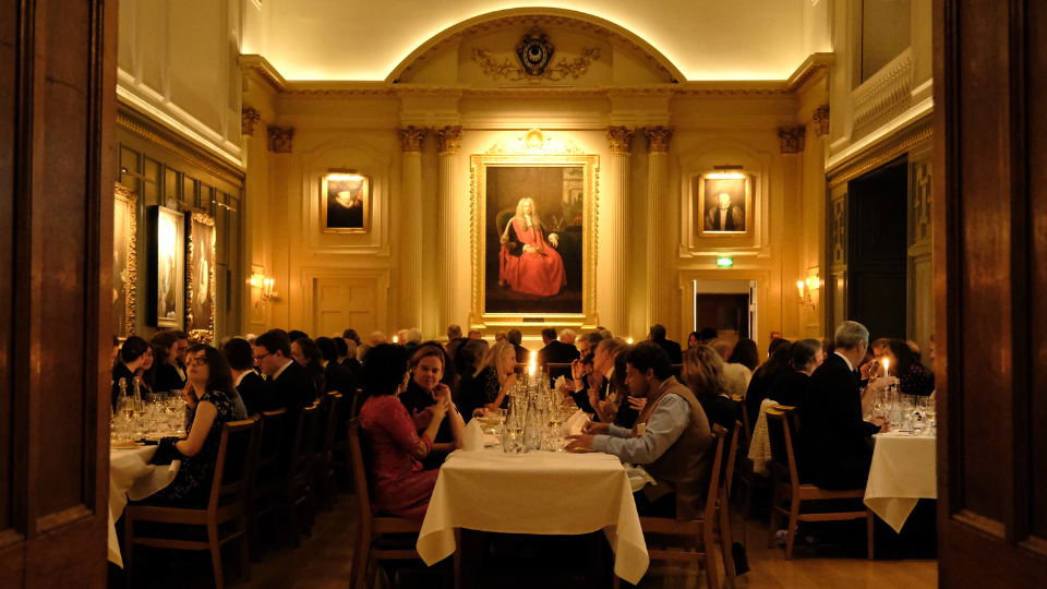 People sit at tables, laid for dinner, in Trinity Hall Dining Hall