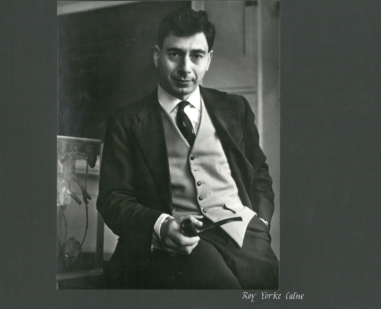 Black and white image of Sir Roy Calne in his early years as a Fellow at Trinity Hall, Cambridge. He is in a jacket with tie and holding a pipe.