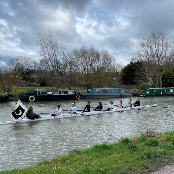 Trinity Hall W2 rowing eight with in the River Cam with the College flag behind, showing that they have won their blades.