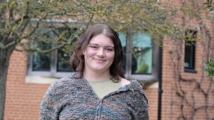 Abby Reeves, winner of the creative writing prize at Trinity Hall. She stands, smiling, outside with the library in the background.