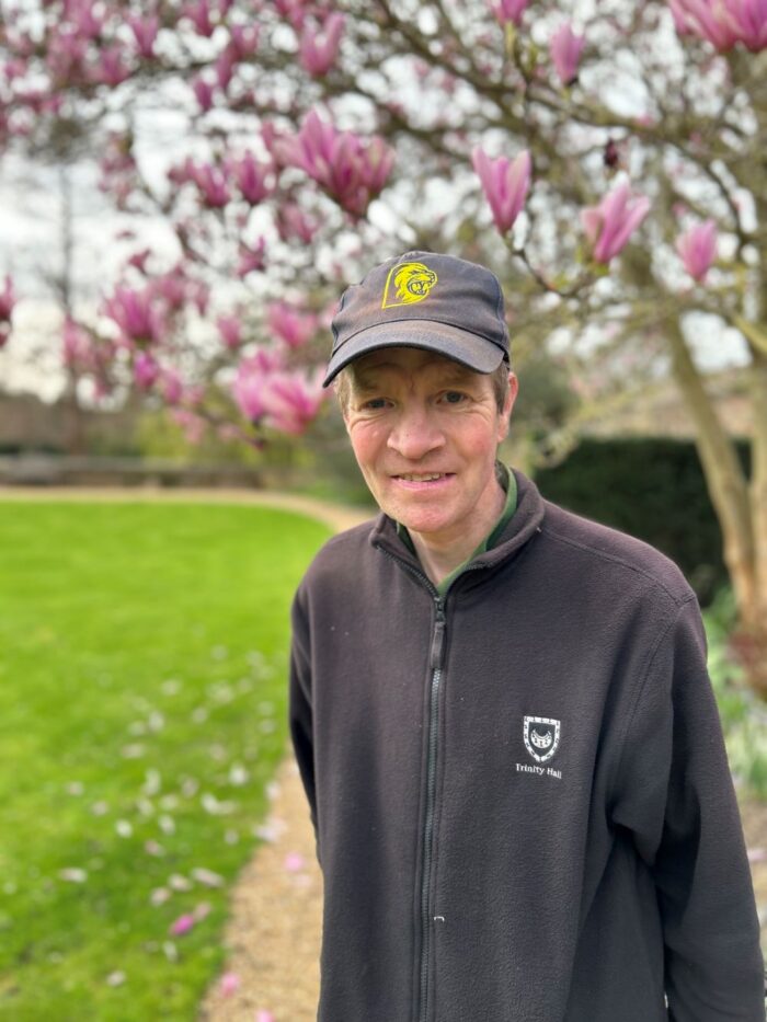 Richard Macarthy stands in the Fellows' Garden at Trinity Hall, Cambridge with a flowering Magnolia tree in the background covered in pink flowers