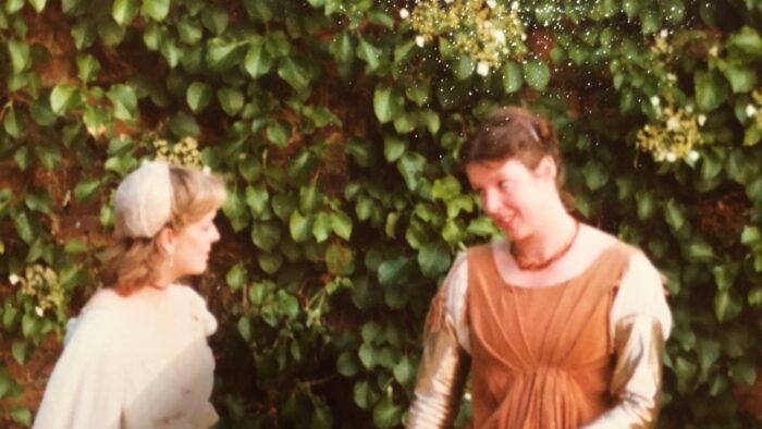 Two women dressed in long Elizabethan dresses, performing as part of a play.