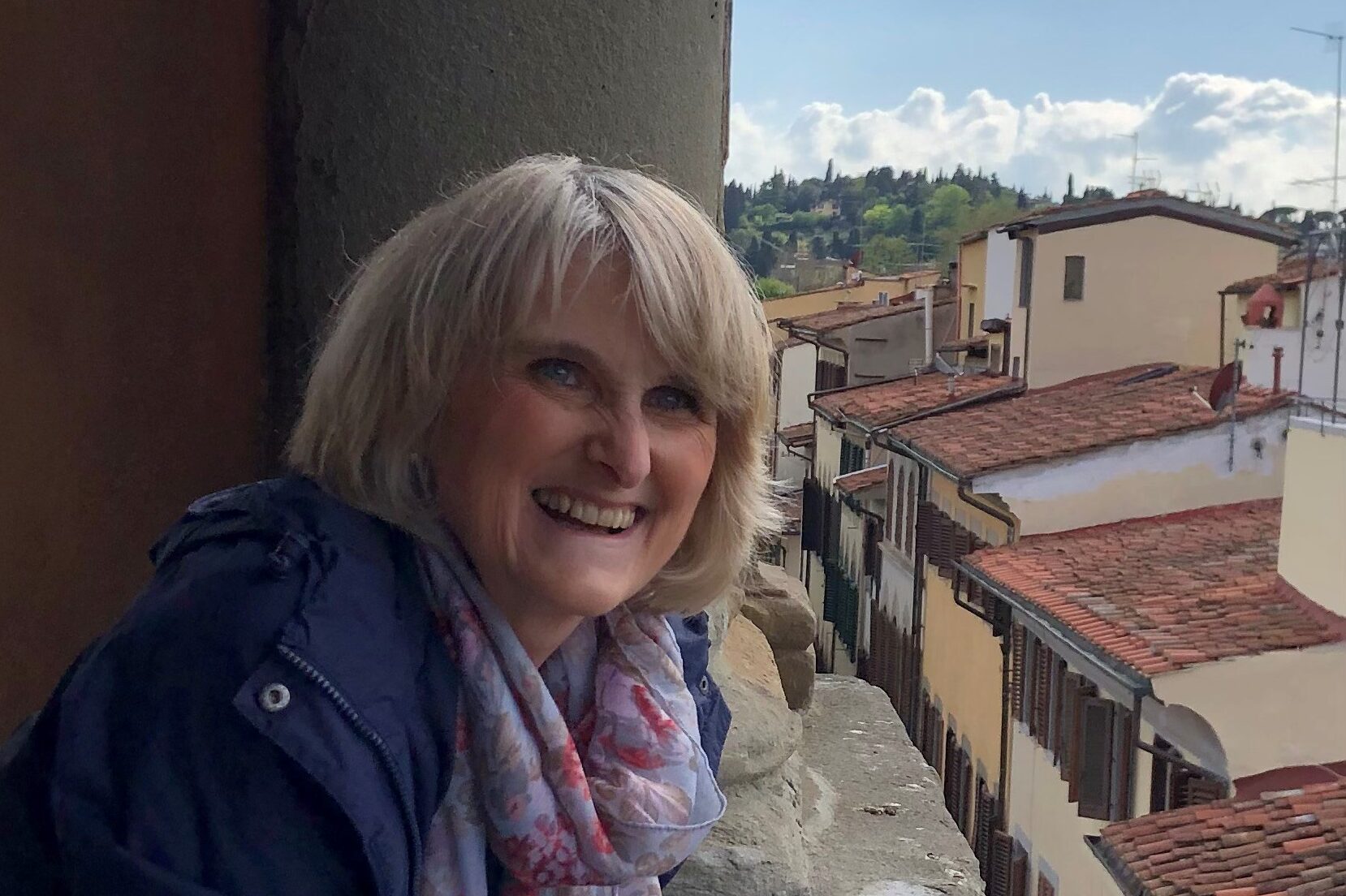 A photograph of a person standing on a balcony, looking out over tiled rooftops and buildings in a town below