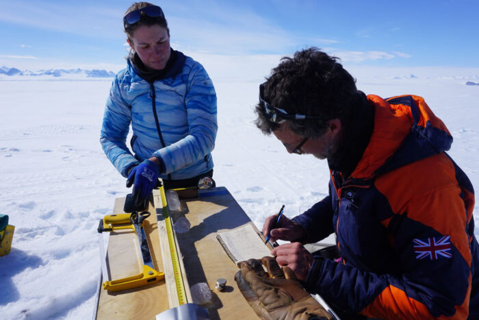 Researchers take measurements and record data during fieldwork on a snow-covered ice shelf.