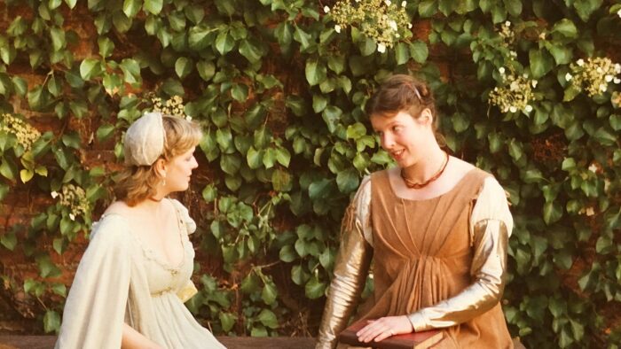 Two women dressed in long Elizabethan dresses, performing as part of a play.