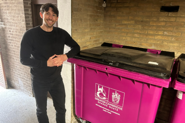 Man leaning on a pink Cambridgeshire County Council bin.