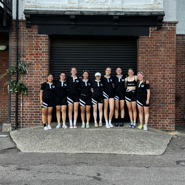 A racing crew in black and white uniforms standing in front of a brick wall.