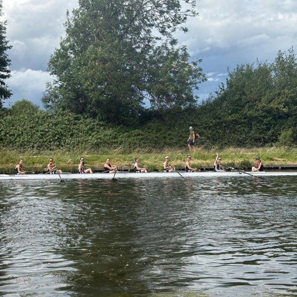 A crew of rowers sitting in a boat holding onto the bank of the river.
