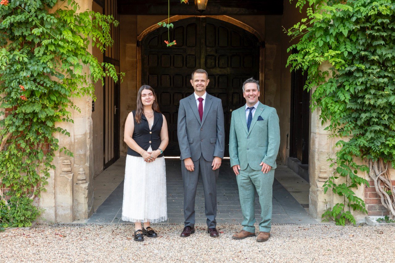 A colour photo of a woman and two men smartly dressed, smiling at the camera.