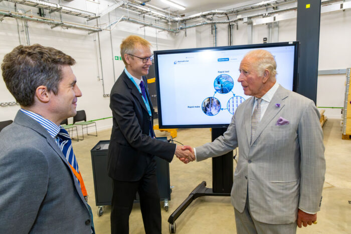 Professor Graham Pullan and His Majesty The King shake hands and smile in front of a screen showing a rapid testing model during the New Whittle Laboratory opening. Photo by Ian Jones.