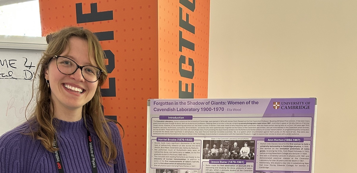 Ella Woods standing beside a poster on women of the Cavendish Laboratory at the PostGraduate Women+ in Physics Conference.