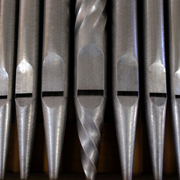 Close-up view of silver organ pipes arranged in a row, including a central pipe with a decorative twisted design.