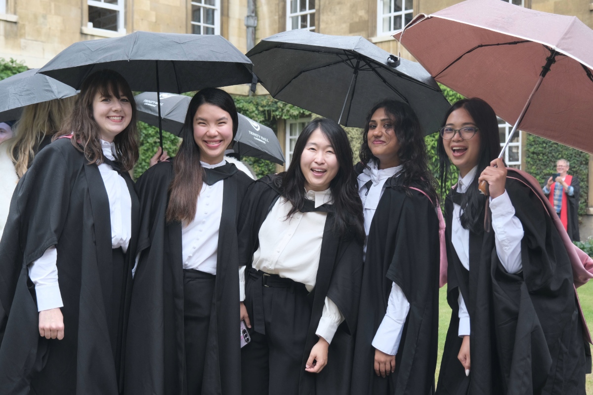 A group of students in academic dress holding umbrellas, standing in a historic court.